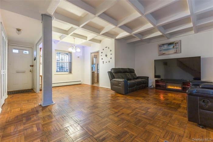 Living area with beamed ceiling, coffered ceiling, a baseboard heating unit, a glass covered fireplace, and a chandelier