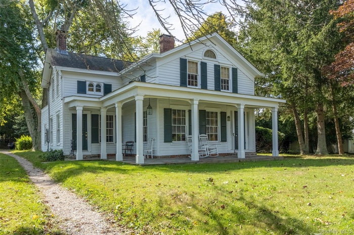 Neoclassical / greek revival house featuring a chimney, a large porch, and a front yard