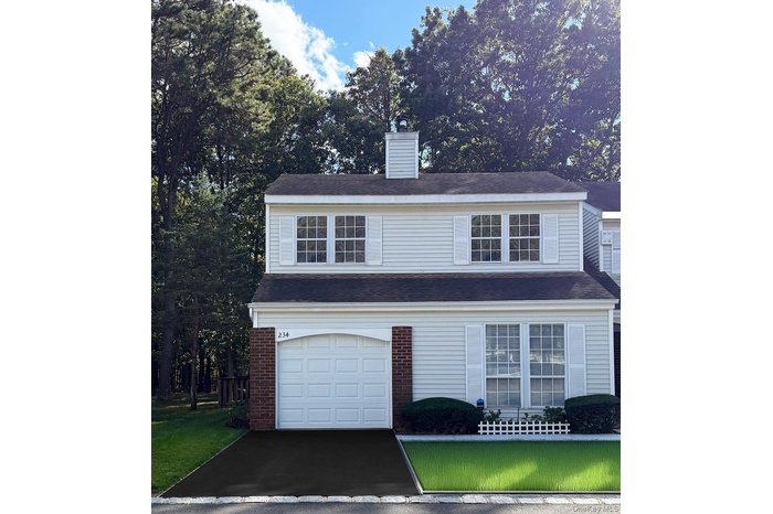 Traditional-style home with a front yard, a chimney, an attached garage, and brick siding