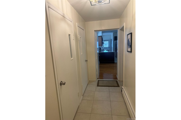 Hallway featuring a baseboard radiator, light tile patterned floors, and a chandelier