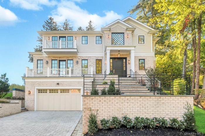 View of front of house with decorative driveway, a garage, a balcony, brick siding, and stairs