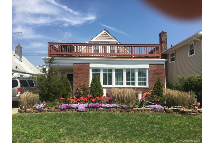 View of front of home featuring a balcony, brick siding, and a front lawn