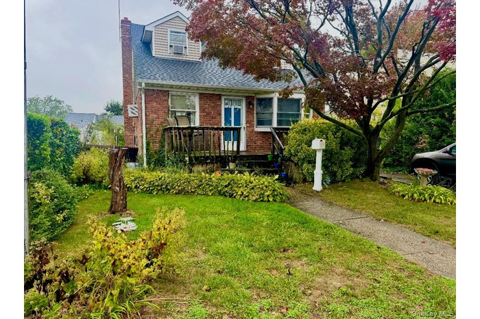 View of front facade with a chimney, a front yard, brick siding, and roof with shingles