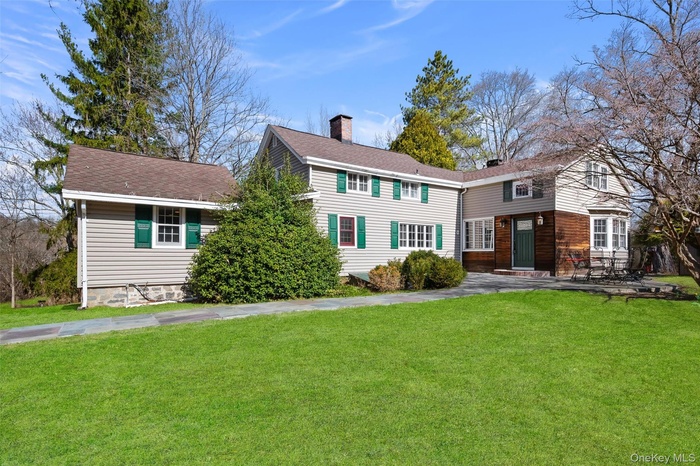 View of front of property featuring a front yard, a shingled roof, and a chimney