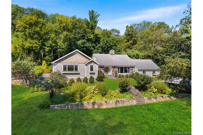 View of front of home featuring a front yard, a chimney, a view of trees, and a porch