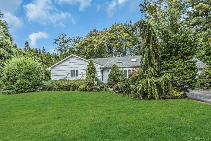 Single story home featuring a front lawn, view of scattered trees, and a shingled roof