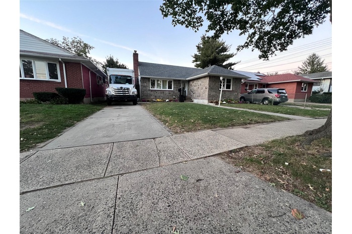 View of front of home featuring a chimney, a front yard, and driveway