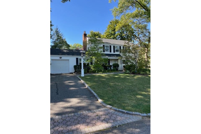 View of front of property with a chimney, a front yard, a garage, and driveway