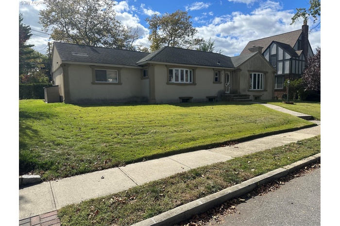 View of front of home featuring a shingled roof, stucco siding, and a front yard