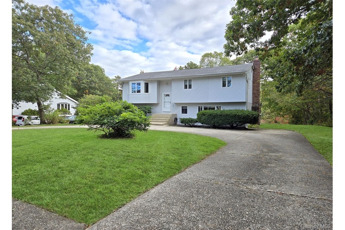 Split foyer home with a chimney, driveway, and a front yard