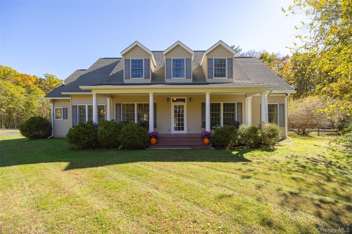 New england style home with a shingled roof, a porch, and a front yard