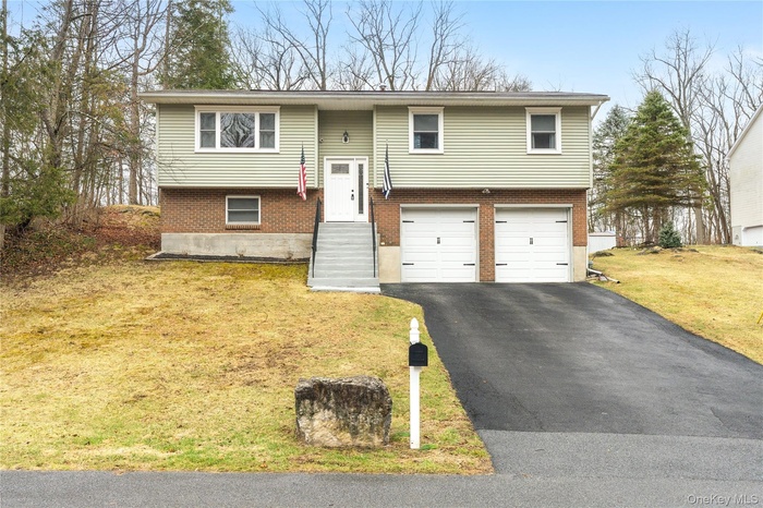 Raised ranch featuring aphalt driveway, brick siding, a garage, and a front yard