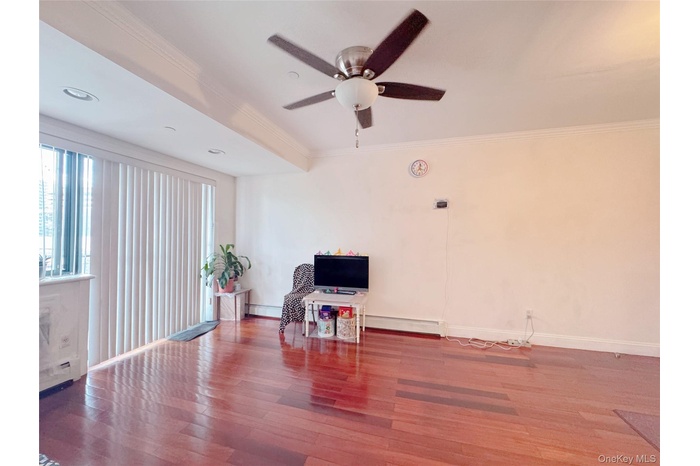 Living area featuring crown molding, wood finished floors, a ceiling fan, and baseboard heating