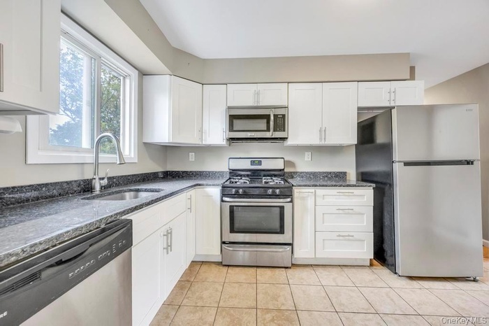 Kitchen with appliances with stainless steel finishes, white cabinets, dark stone countertops, and light tile patterned flooring
