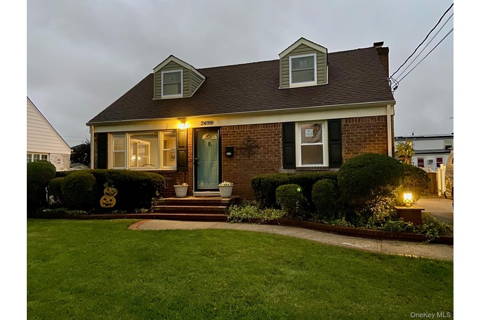 Cape cod home with a front yard, brick siding, and roof with shingles
