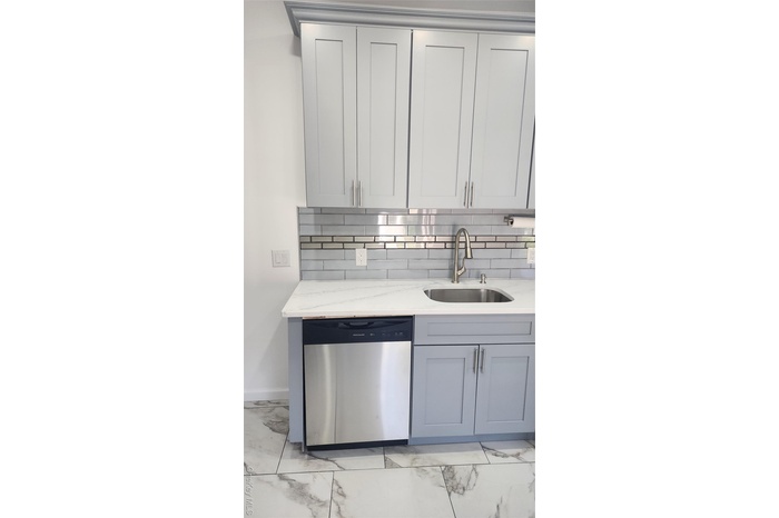 Kitchen featuring light marble finish flooring, dishwashing machine, gray cabinetry, light stone counters, and tasteful backsplash