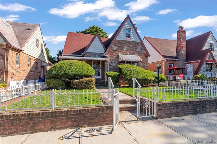 Tudor-style house featuring a fenced front yard, brick siding, and a gate