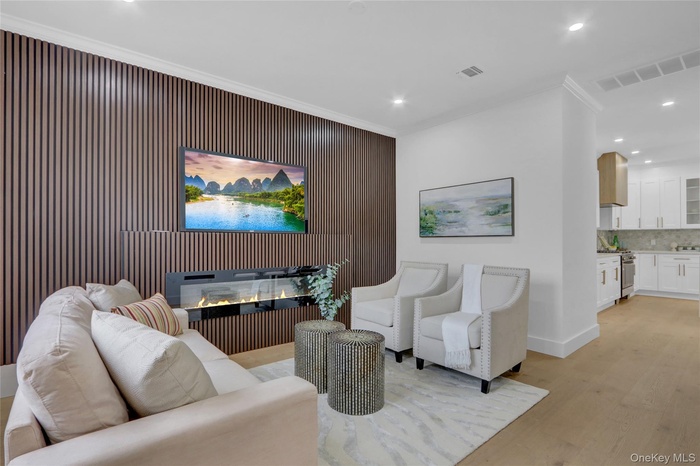 Living room with light wood-style floors, crown molding, recessed lighting, an accent wall, and a glass covered fireplace