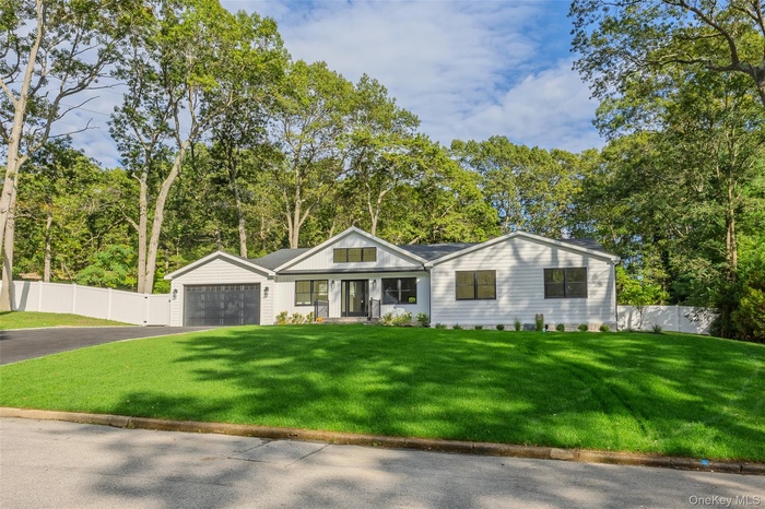 View of front facade featuring driveway, a garage, view of scattered trees, and covered porch