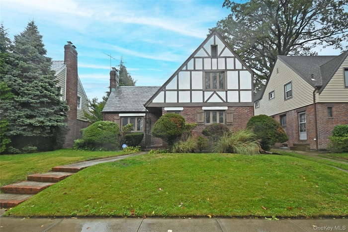 Tudor-style house with brick siding, stucco siding, a front yard, and a chimney