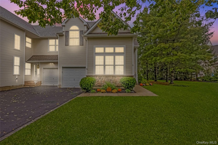 Traditional-style home featuring driveway, a garage, stone siding, and a lawn
