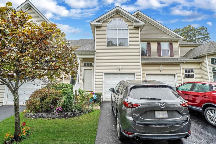 Traditional home featuring an attached garage, roof with shingles, asphalt driveway, and a front yard