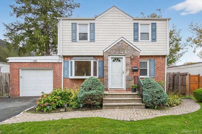 Colonial house featuring an attached garage, asphalt driveway, and brick siding