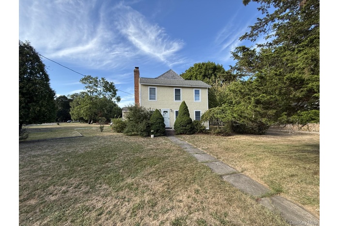 Colonial inspired home with a chimney, a front yard, and a shingled roof