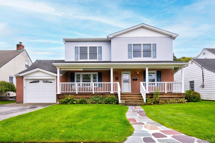 View of front facade featuring a porch, a front lawn, brick siding, and a garage