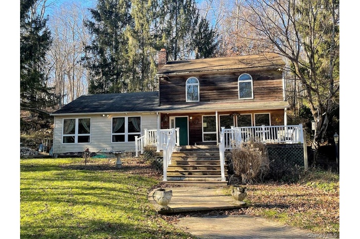 View of front facade with a chimney, a porch, a front yard, and stairs
