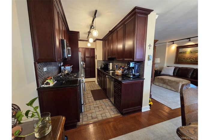 Kitchen featuring track lighting, backsplash, appliances with stainless steel finishes, open floor plan, and ornamental molding