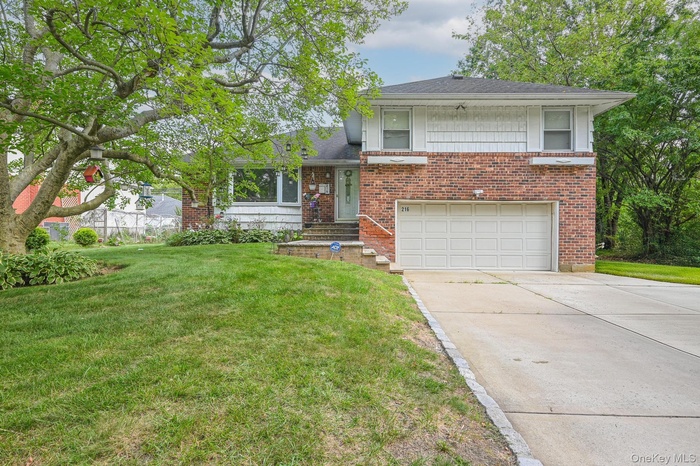 Split level home with a garage, driveway, a front lawn, brick siding, and roof with shingles