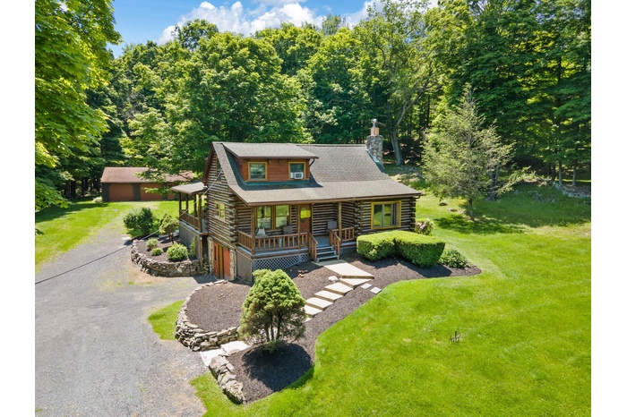 Cabin with log exterior, a porch, a chimney, driveway, and a front yard