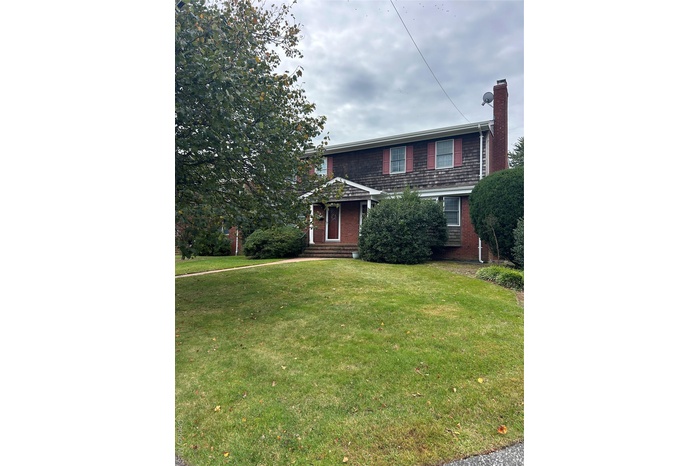 Traditional-style home with a chimney, a front yard, entry steps, and brick siding