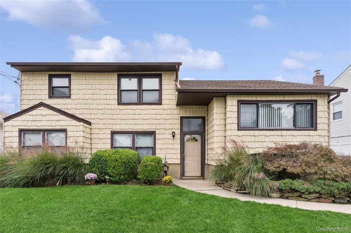 View of front of house featuring a chimney, a front yard, and a shingled roof