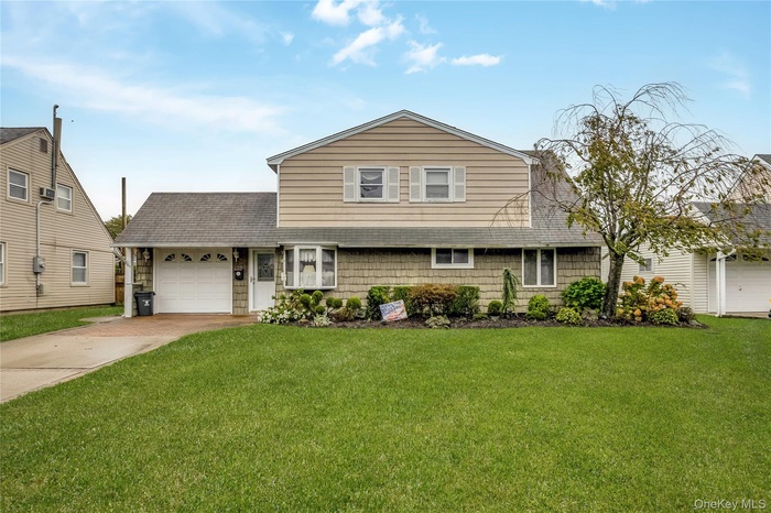 View of front of property featuring a shingled roof, a front yard, concrete driveway, and an attached partial garage