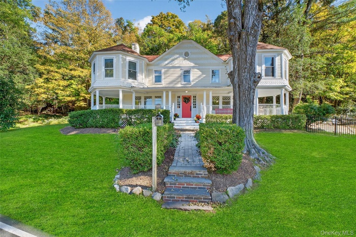 Victorian house featuring a porch, a front yard, a chimney, and view of wooded area