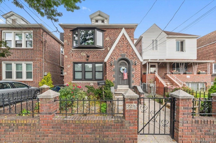 Tudor house featuring a fenced front yard, a gate, brick siding, and a porch