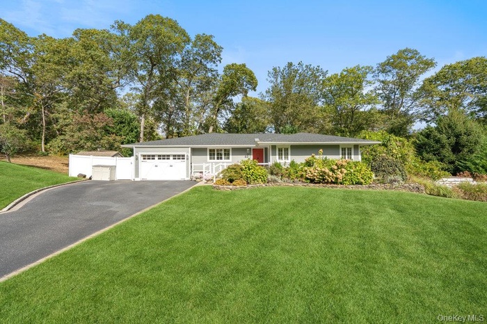 Ranch-style home with a front yard, asphalt driveway, and view of scattered trees