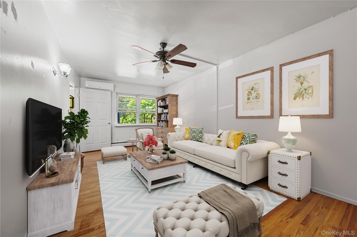 Living area featuring light wood-style floors, ceiling fan, and a wall unit AC