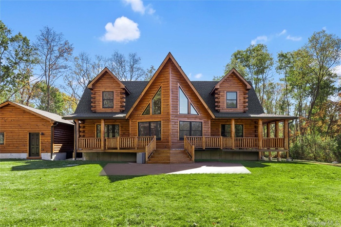 Rear view of property featuring a porch, a lawn, and roof with shingles