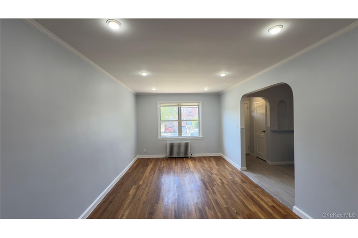 Spare room featuring crown molding, arched walkways, wood finished floors, radiator, and recessed lighting