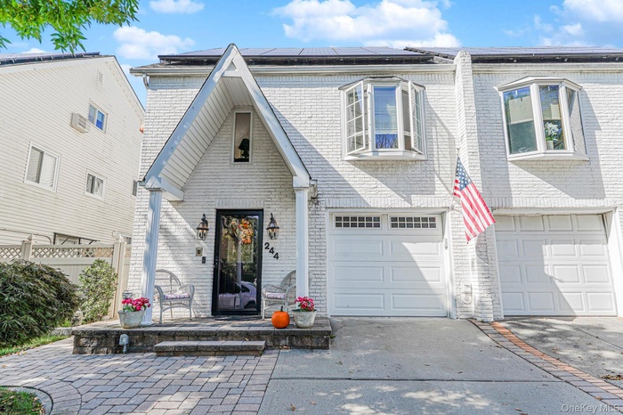 View of front facade with driveway, brick siding, roof mounted solar panels, and an attached garage