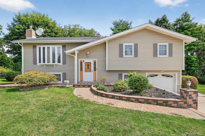 Bi-level home featuring a front yard, an attached garage, and a chimney