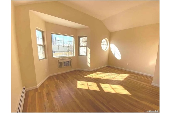 Unfurnished room with a baseboard heating unit, light wood finished floors, vaulted ceiling, and a wall unit AC