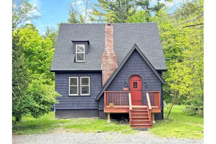 View of front of property featuring roof with shingles, a chimney, and a deck