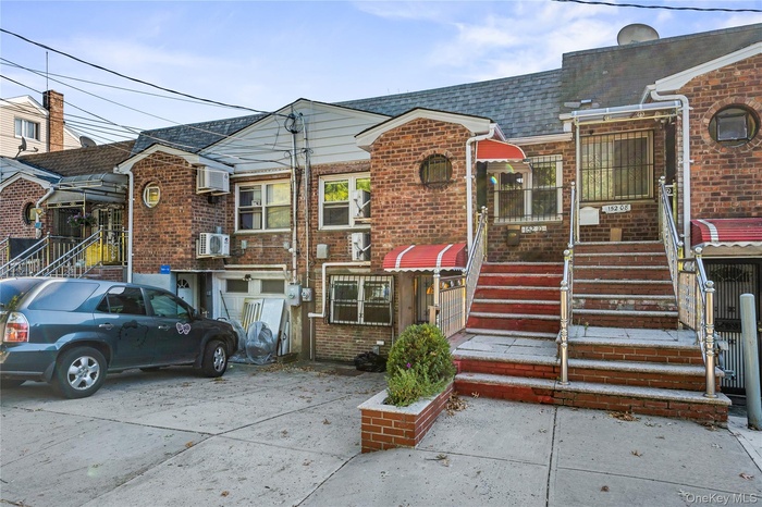 View of front of house with a shingled roof, brick siding, and a wall unit AC