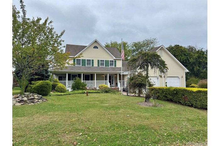 Farmhouse with covered porch, a front yard, a garage, and a shingled roof