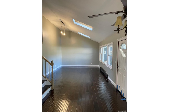 Foyer with stairway, lofted ceiling, dark wood finished floors, and a skylight