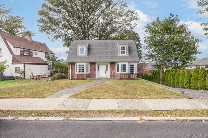 Colonial inspired home with brick siding, roof with shingles, and a front yard